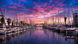 A marina with multiple boats docked, calm water, and a sunset sky. - Hôtel des 2 golfs (Leucate)