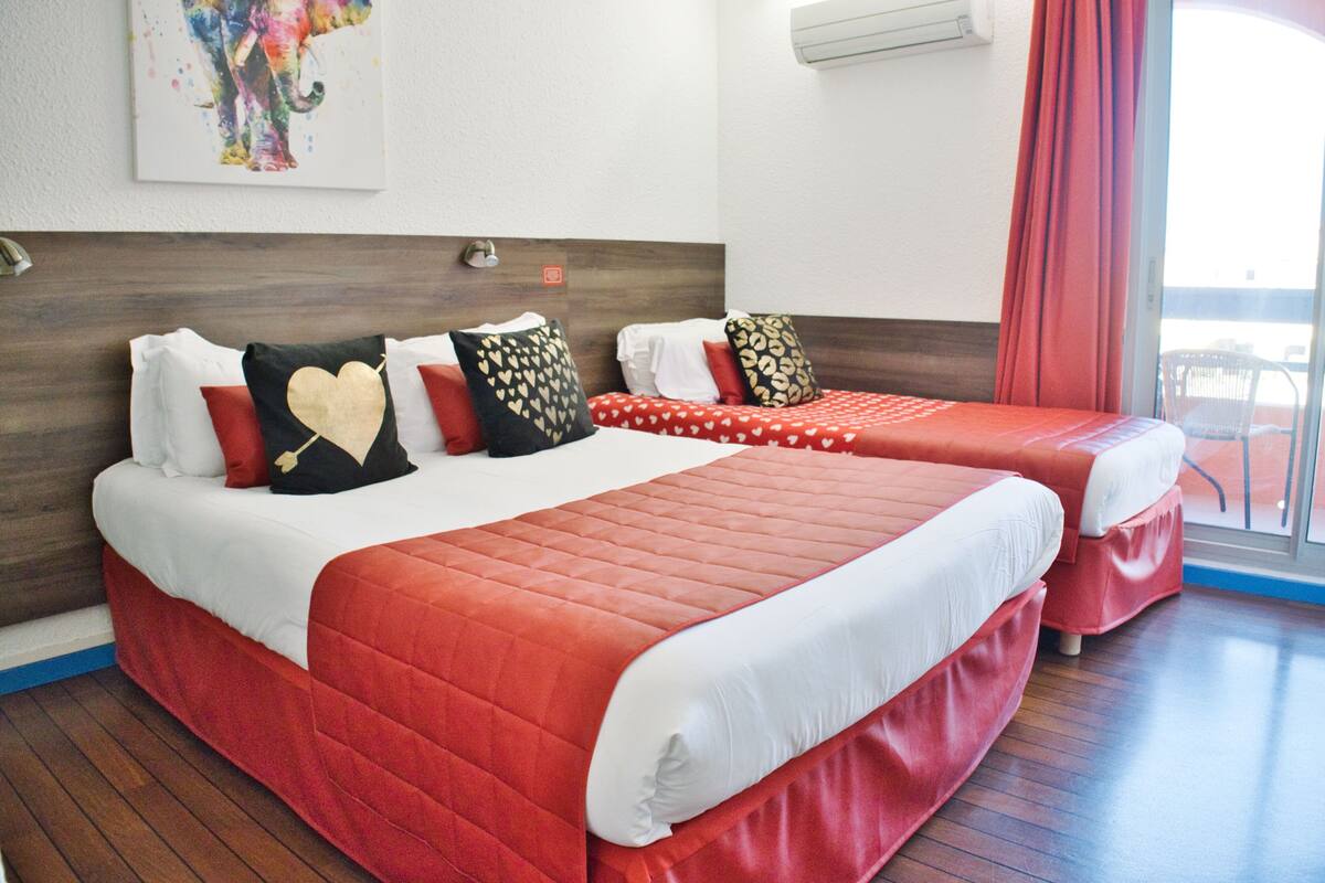 A hotel room with two beds, each with red bedding and heart-shaped pillows.