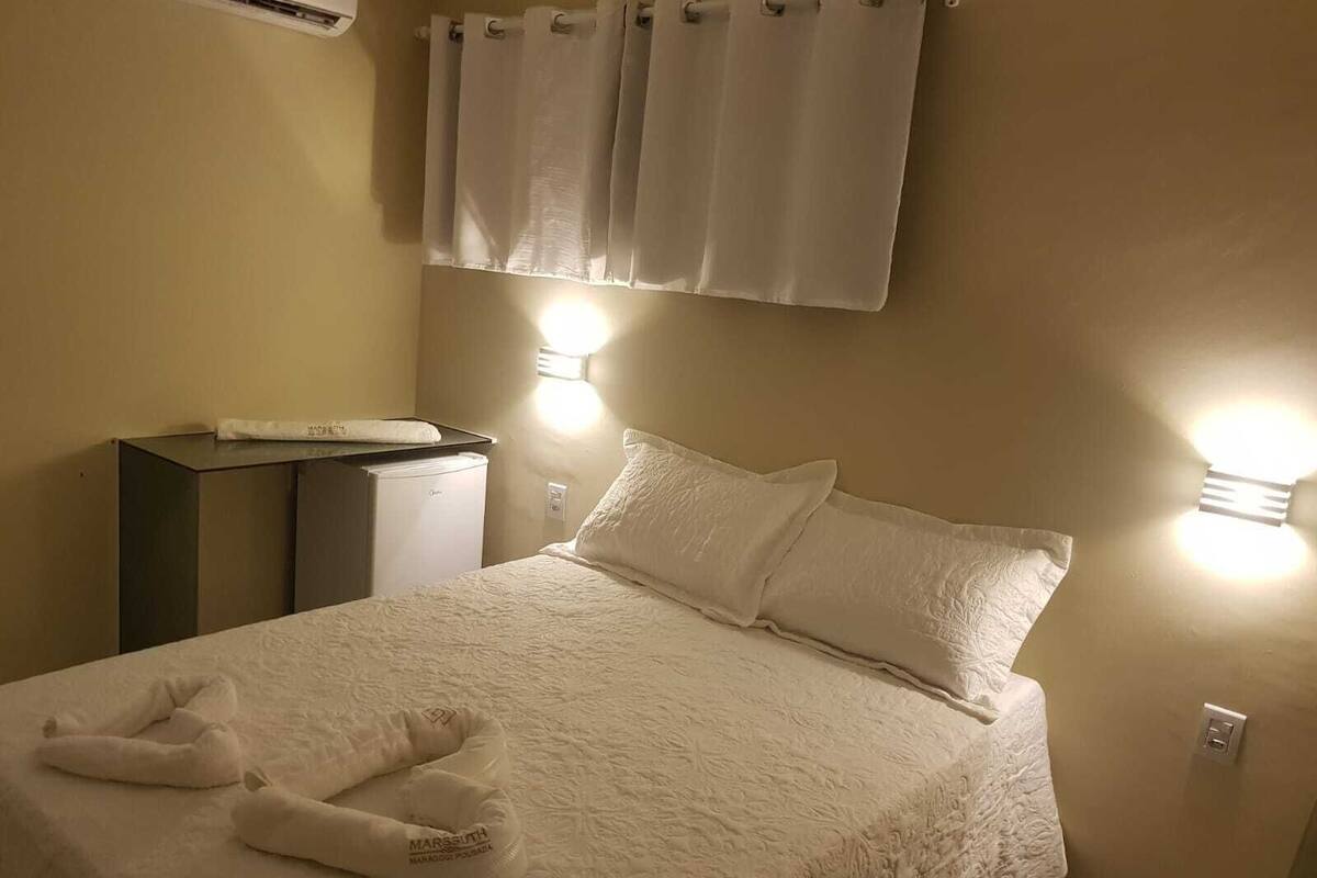 Une chambre d’hôtel avec un lit, un bureau équipé d’un ordinateur et deux lampes fixées au mur.