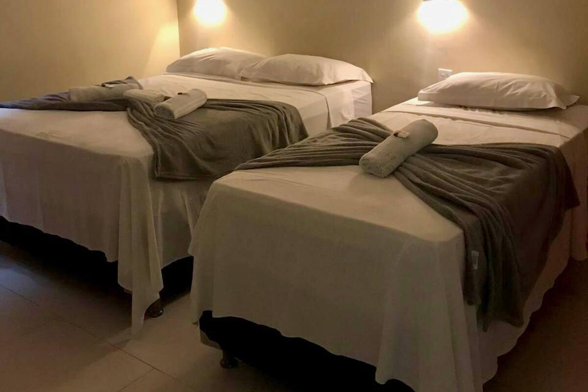 Une chambre avec deux lits simples, chacun équipé d’un oreiller et d’une couverture. Deux lampes murales sont fixées de part et d’autre des lits.