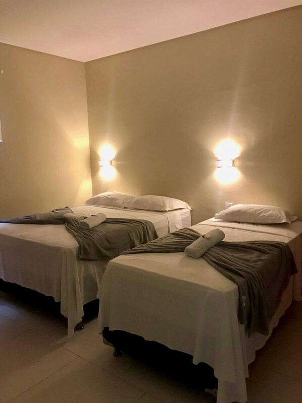A room with two single beds, each with a pillow and a blanket. There are two wall-mounted lights on either side of the beds. - Marssuth Pousada (Maragogi)