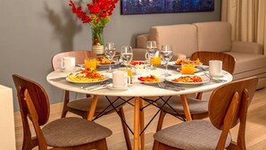 A dining area with a round table set for breakfast, including plates of food, glasses, and a vase of red flowers. - Tú Paraiso privado - Lahun suites Playa del Carmen  (Playa del Carmen)