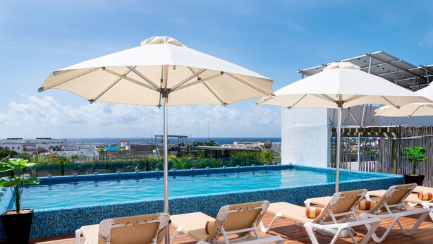 A rooftop pool area with lounge chairs and umbrellas, a view of the ocean, and a tiled pool. - Tú Paraiso privado - Lahun suites Playa del Carmen  (Playa del Carmen)