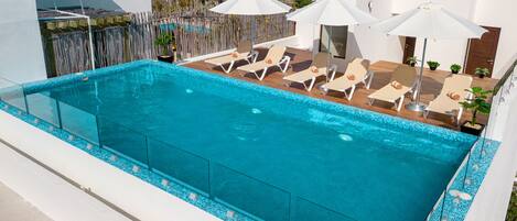 Una piscina al aire libre, sombrillas, sillones reclinables de piscina