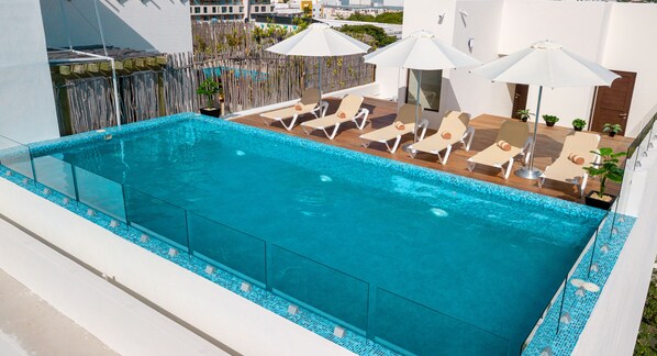 Una piscina al aire libre, sombrillas, sillones reclinables de piscina