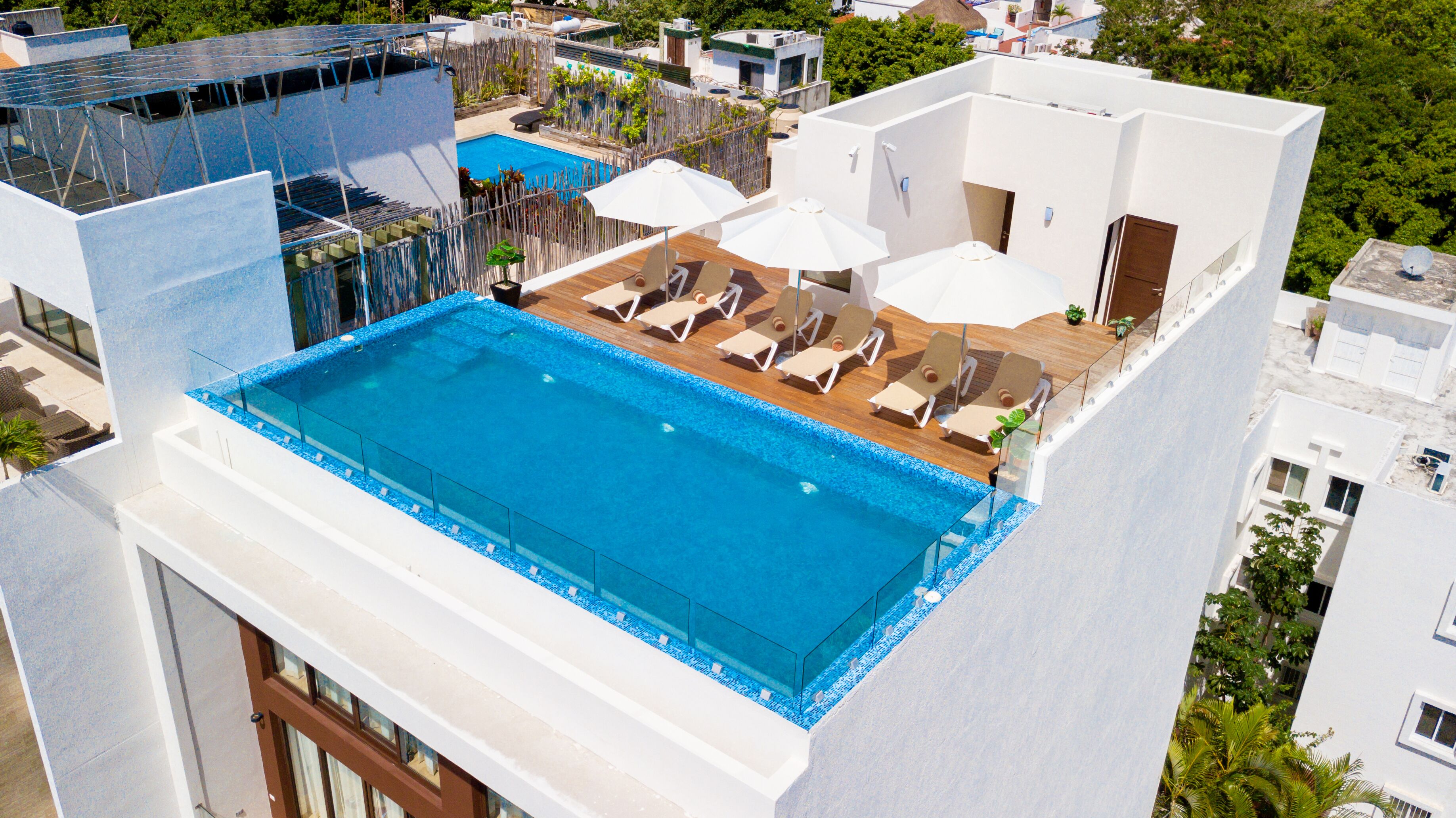 Ein Dachpool mit Liegestühlen und Sonnenschirmen, umgeben von weißen Gebäuden und viel Grün.