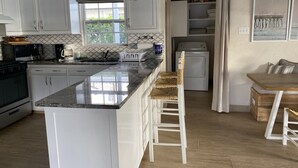 Eine Küche mit weißen Schränken, einer Granitarbeitsplatte, einem eingebauten Backofen, einer Mikrowelle, einer Kaffeemaschine und einer Pendelleuchte.