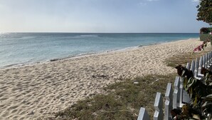 Ein Strand mit weißem Zaun, sandigem Ufer und blauem Himmel.