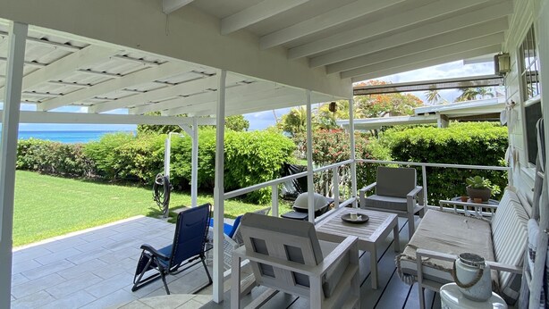 Eine überdachte Terrasse mit Sitzgelegenheiten im Freien, Blick auf den Ozean und einem gepflegten Rasen.