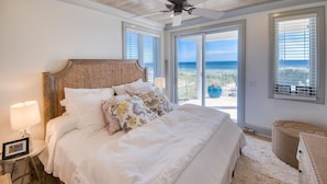 Ein Schlafzimmer mit einem großen Bett, einem Deckenventilator und Blick auf den Strand durch die Fenster.