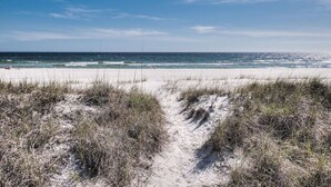 Ein Strand mit einem sandigen Pfad, der zum Meer führt, unter blauem Himmel.