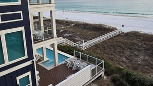 Ein modernes mehrgeschossiges Gebäude mit Pool, weißen Geländern und Blick auf Strand und Meer.
