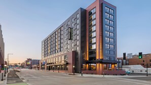 A modern multi-story hotel with a prominent corner entrance, large windows, and a visible sign for 'Hilltop Suites'.