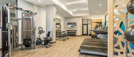 Un gimnasio moderno con equipo de cardio, máquinas de pesas y una variedad de mancuernas.