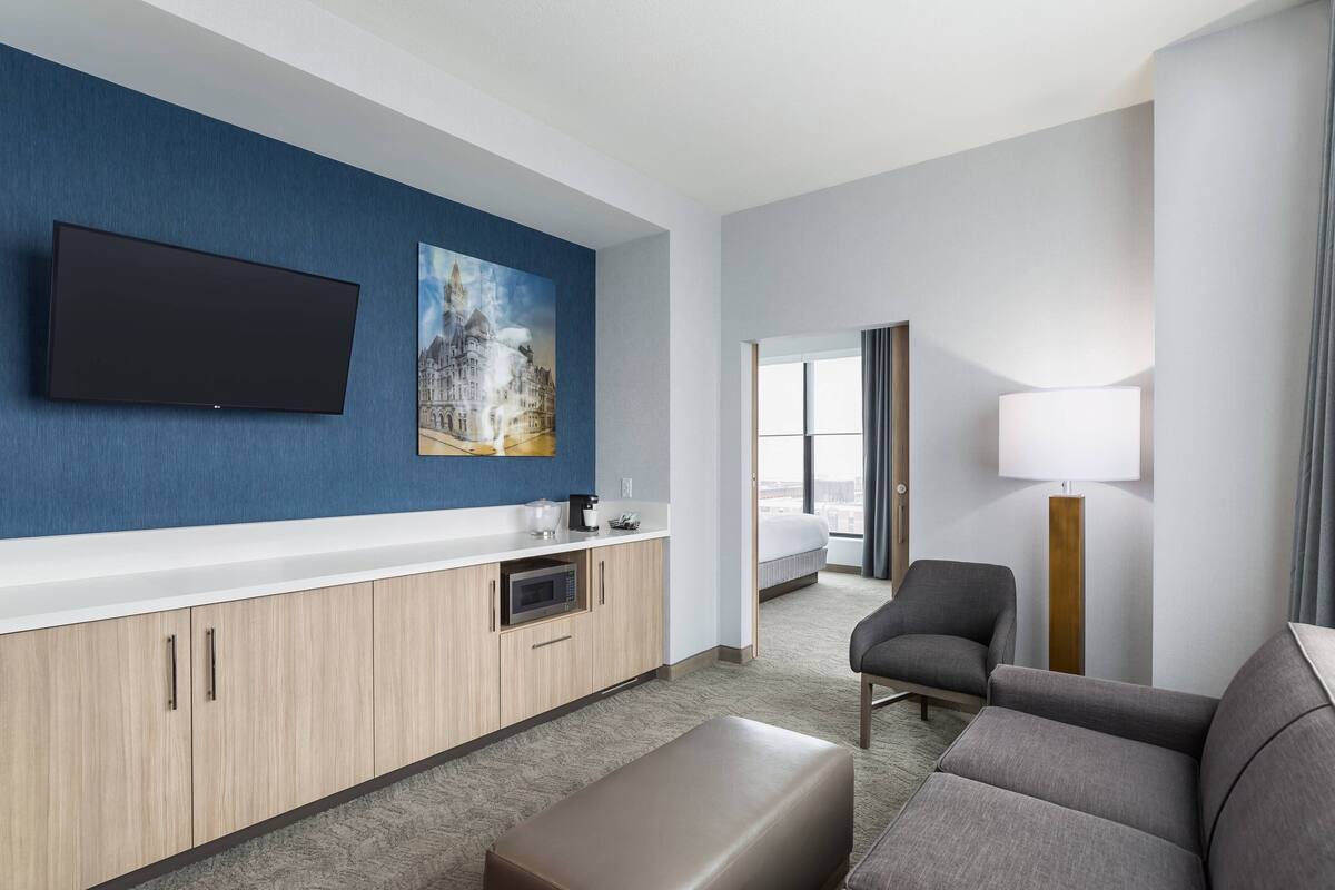 A modern hotel room with a flat-screen TV, a painting, a sofa, a lamp, and a bed.