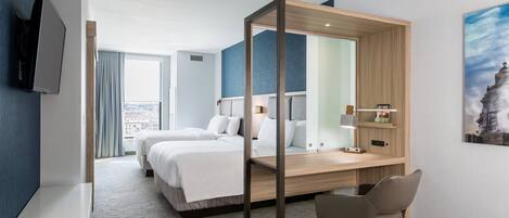 A modern hotel room with a large bed, a desk with a chair, a TV, and a city view.