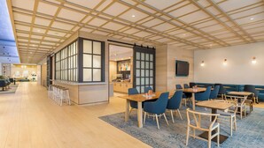 A spacious dining area with wooden tables and chairs, a large window, and a modern ceiling design.