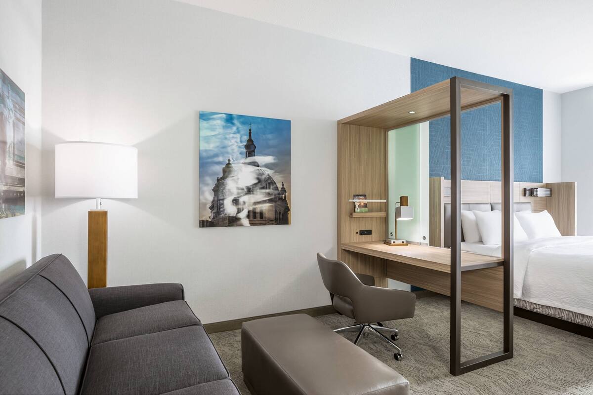 A hotel room with a sofa, desk, chair, and bed.