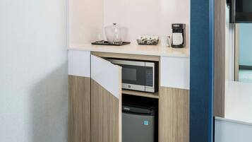 A compact kitchenette with a microwave, coffee maker, and storage containers.