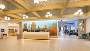 A spacious lobby with a reception desk, modern chandeliers, and a cityscape mural.