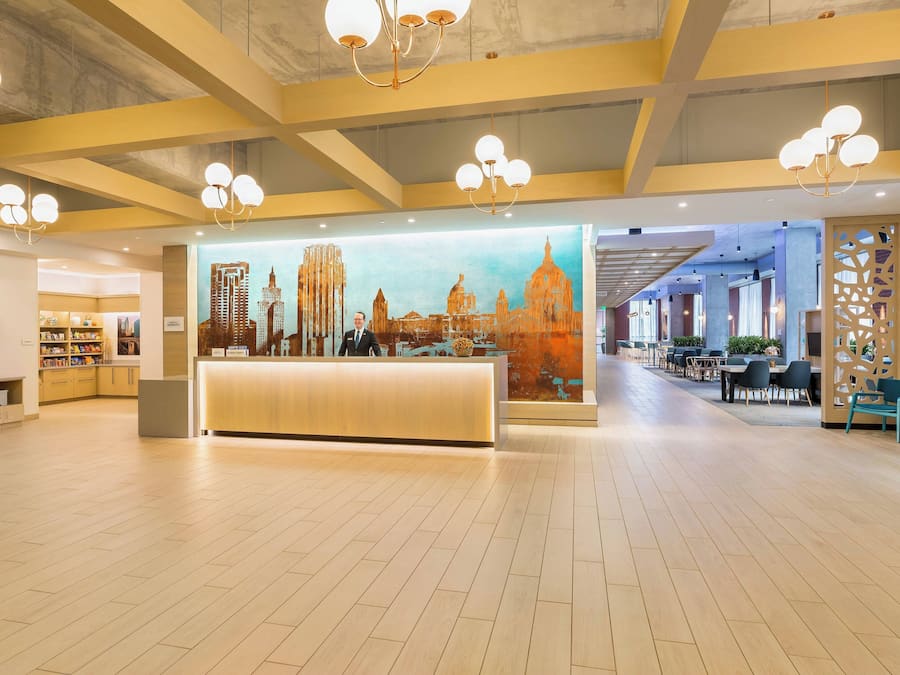 Un vestíbulo amplio con mostrador de recepción, candelabros modernos y un mural con vista a la ciudad.
