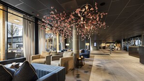 A modern hotel lobby with seating areas, large windows, and a decorative tree installation. - Lily Country Club (Ullensaker)
