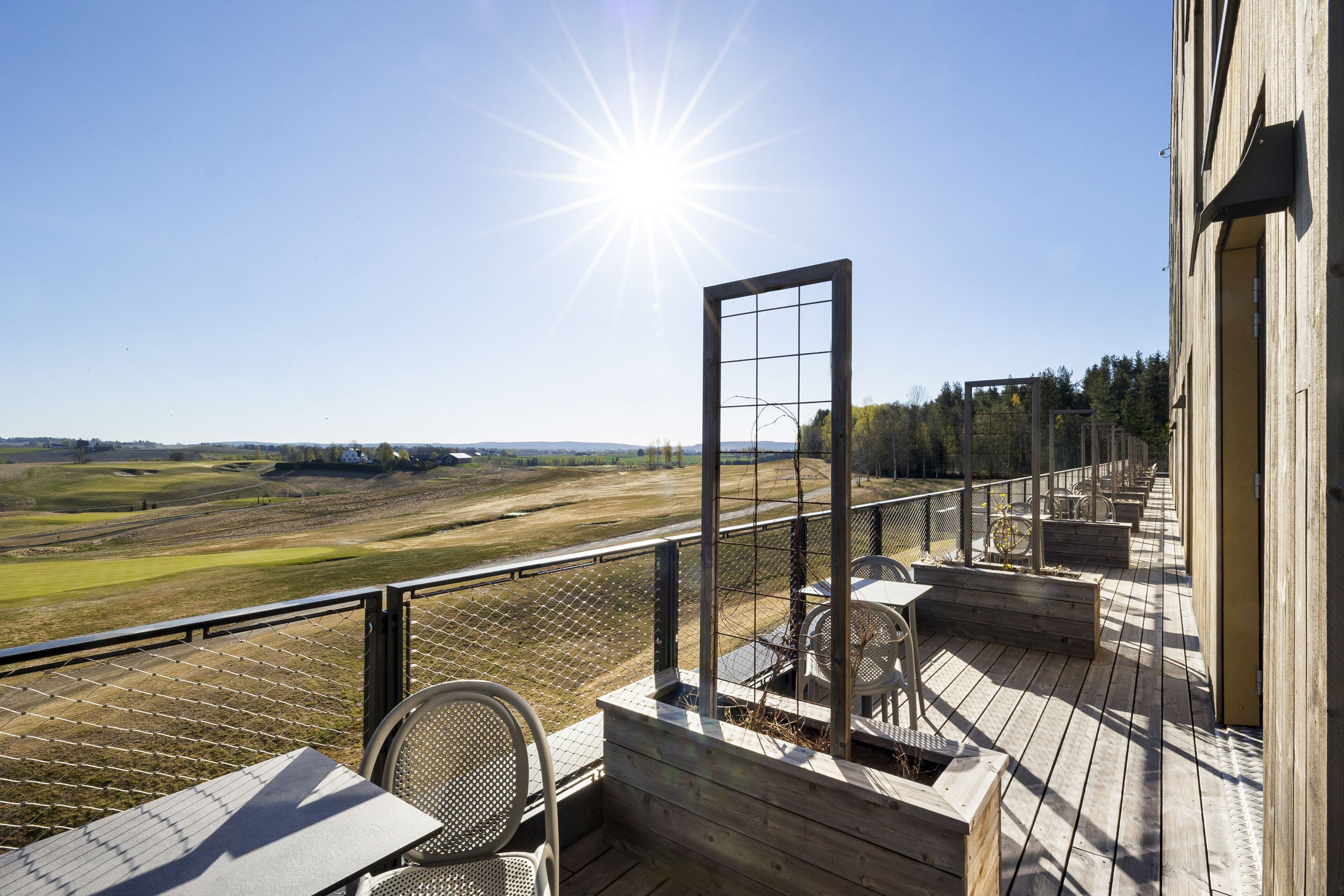 Una terraza de madera con vistas a un viñedo, una mesa y sillas.