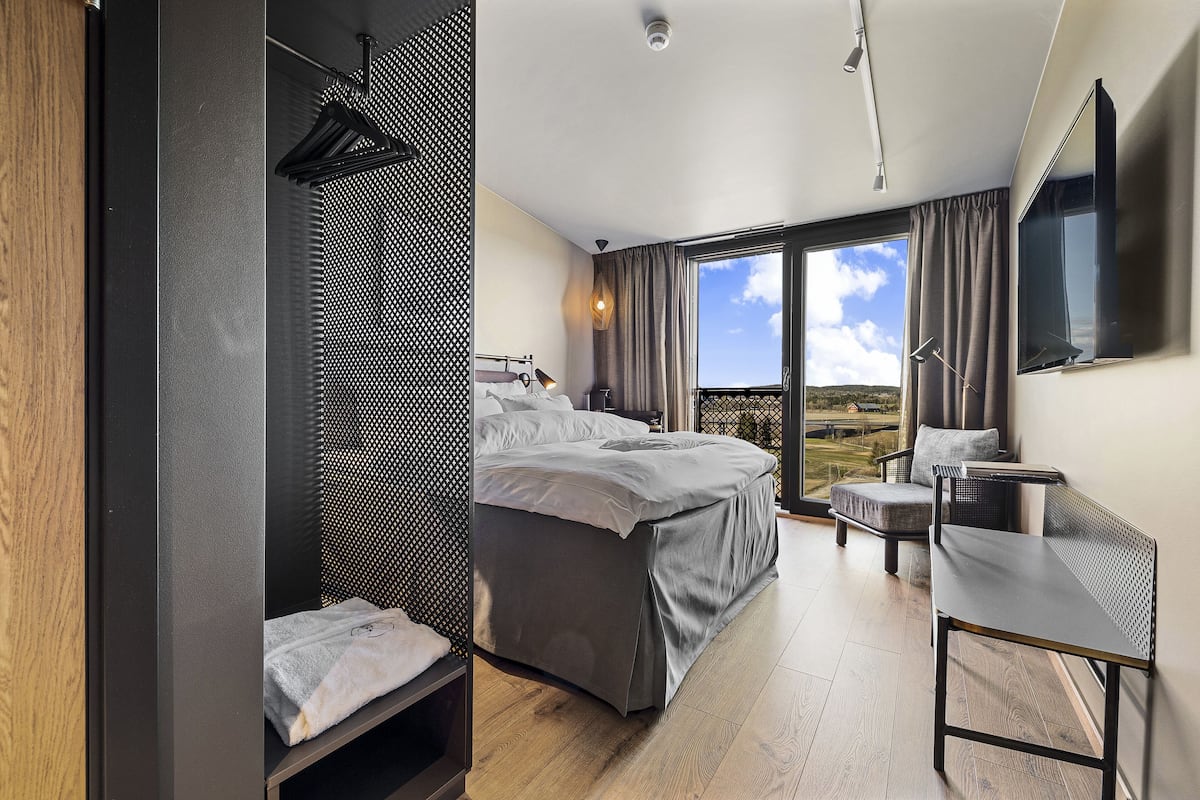 A modern hotel room with a large bed, a seating area, and a balcony with a view.
