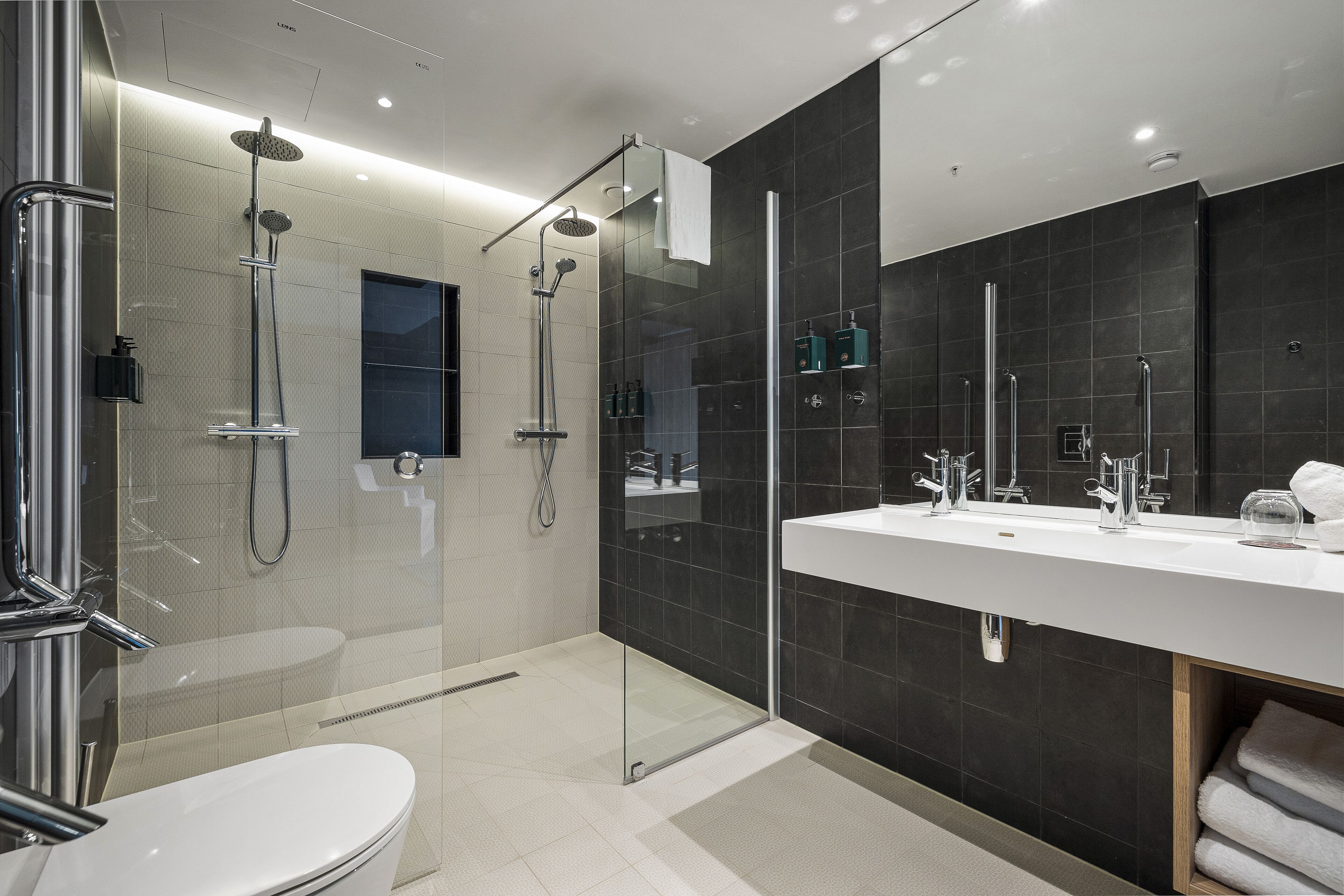 A modern bathroom with a glass-enclosed shower, a white sink, and a large mirror.