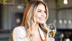 A person seated at a table with a glass of white wine, a bowl of salad, and a bottle of wine on the table. - Lily Country Club (Ullensaker)