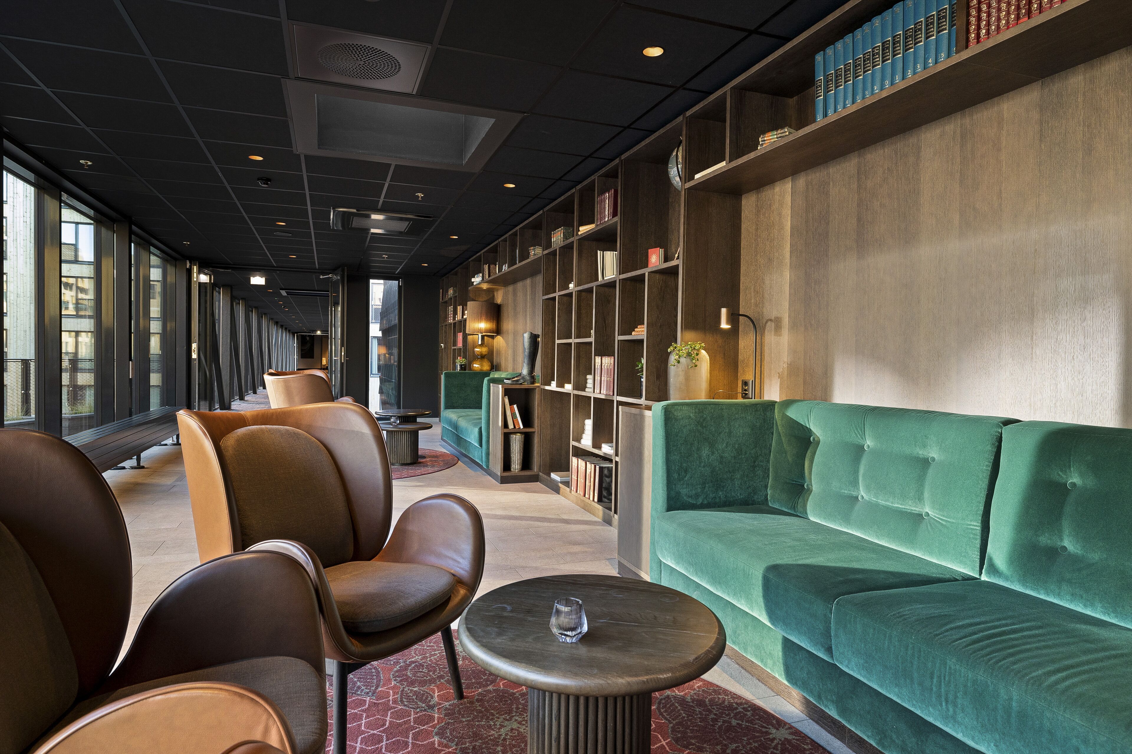 A modern lounge area with leather chairs, a green sofa, and a bookshelf filled with books.