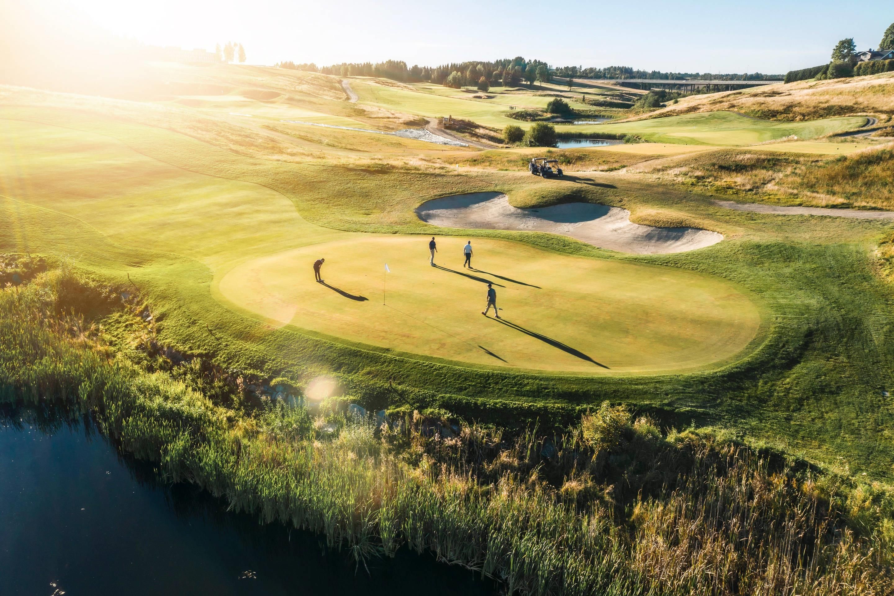 Campo de golf con obstáculo acuático, bunkers de arena y un puente al fondo.