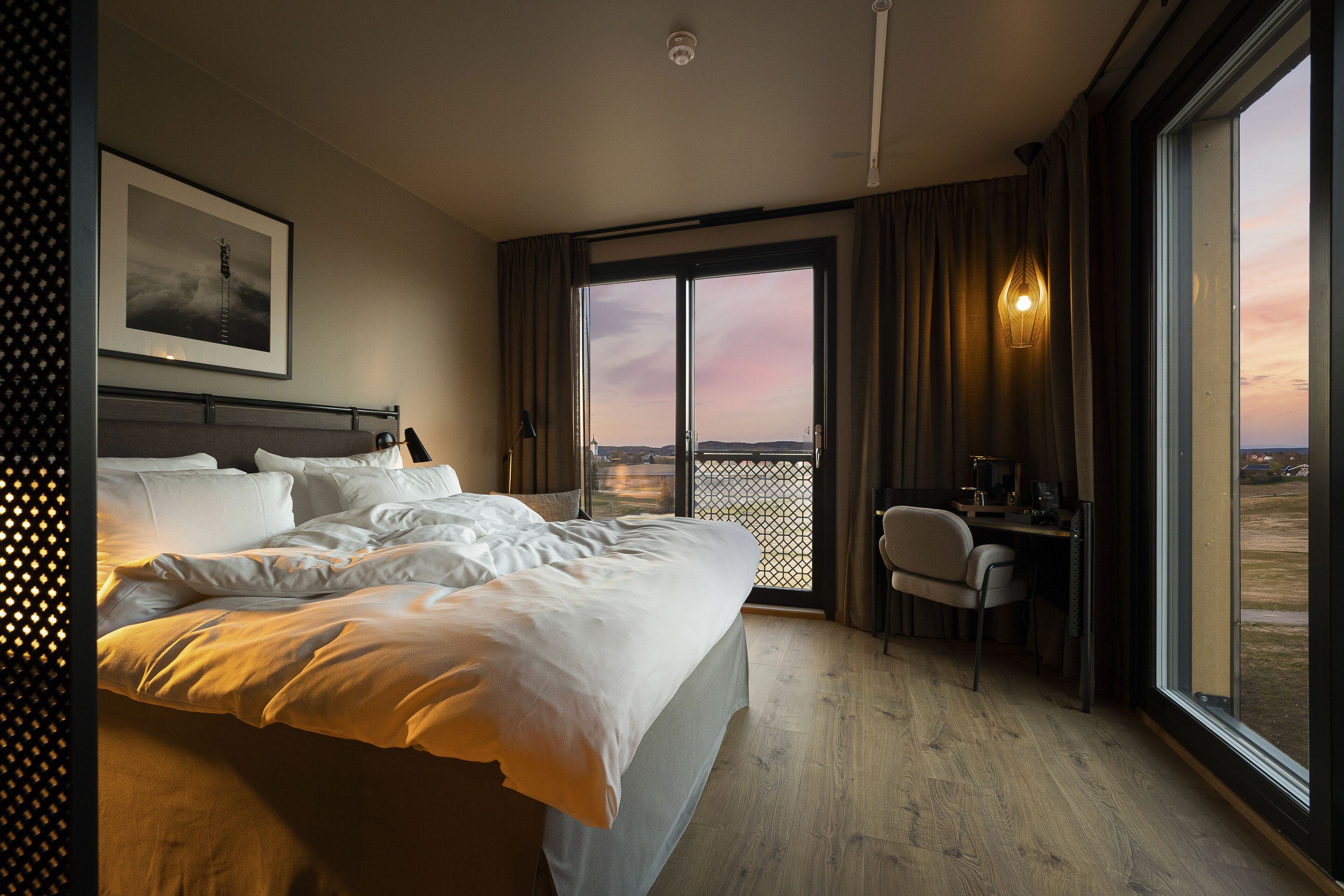 Hotellihuone, jossa on suuri sänky, työpöytä ja ikkunasta avautuva näkymä kaupungin ylle.