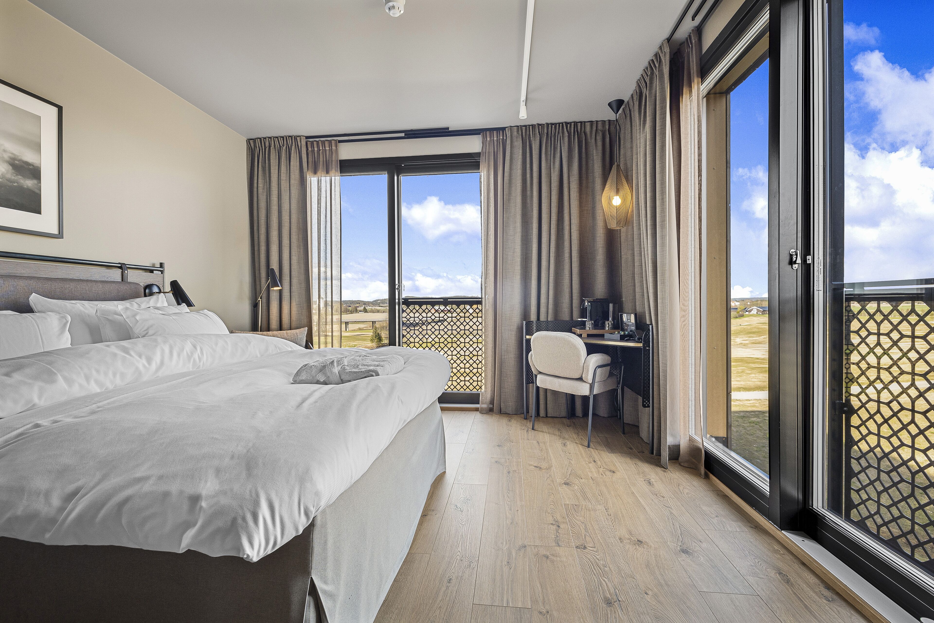 A hotel room with a large bed, a desk, and a balcony with a view.