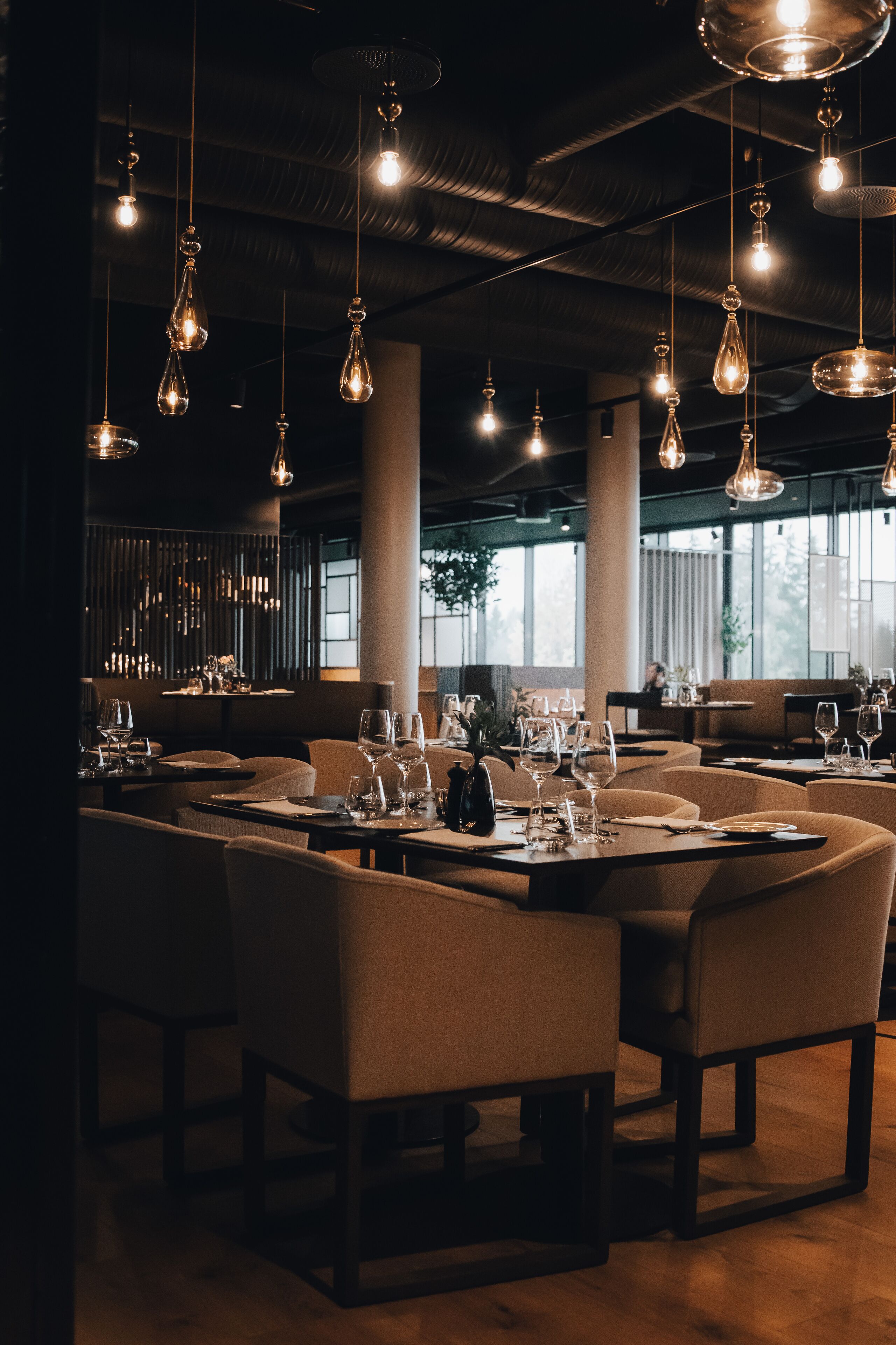 Un restaurante con varias mesas, lámparas colgantes y amplias ventanas.