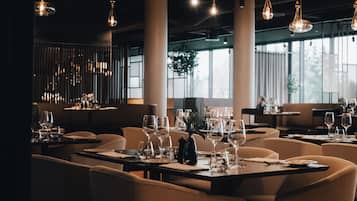 Un restaurante con varias mesas, lámparas colgantes y amplias ventanas.