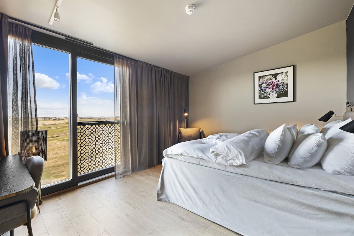 A bedroom with a large bed, a desk, and a view of a field through a sliding door.