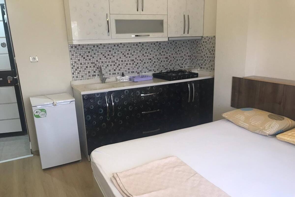 A compact bedroom with a bed, a small kitchenette, and a microwave.