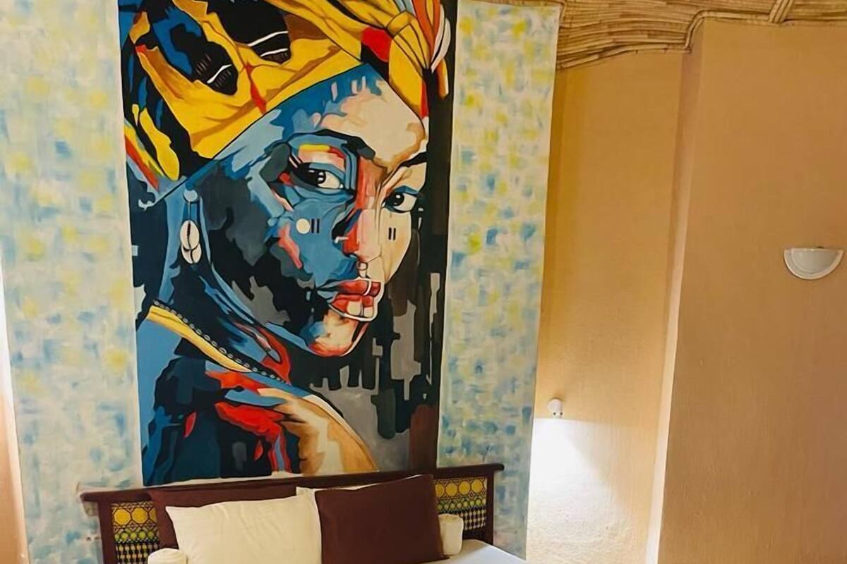A bedroom with a bed, a bench, and a large painting on the wall.