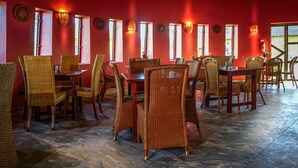 A restaurant with wicker chairs and tables, red walls, and decorative wall lights. - Bamboo Village Resort (Serrekunda)