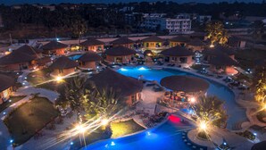 A resort with multiple thatched-roof villas, a central swimming pool, and outdoor seating areas. - Bamboo Village Resort (Serrekunda)