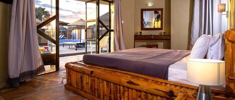 Un dormitorio con una cama grande, cabecera de madera, mesita de noche, lámpara y vistas al exterior a través de una puerta de cristal.