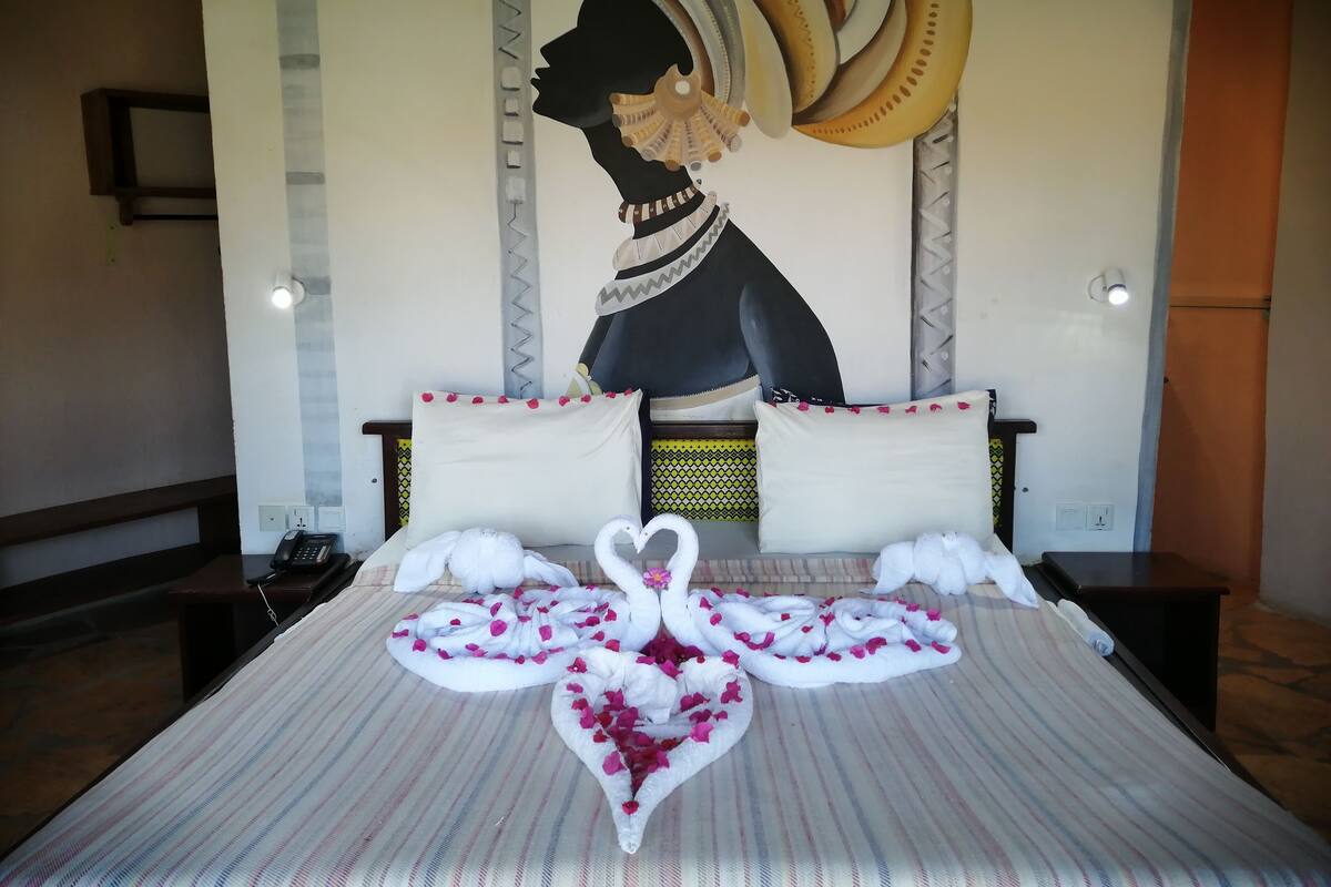 A hotel room with a bed featuring a decorative swan towel arrangement, a large mural on the wall, and a telephone on the nightstand.