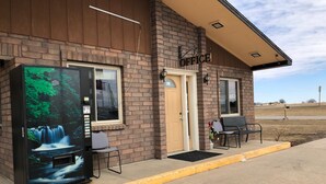 A building with a sign reading "OFFICE" above the entrance. There is a bench and a chair outside. - Rose Motel (David City)