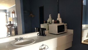 A bathroom with a white sink, a mirror, a microwave, and a towel rack. - Rose Motel (David City)