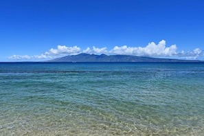 A clear view of a beach with shallow water and a mountain in the background.