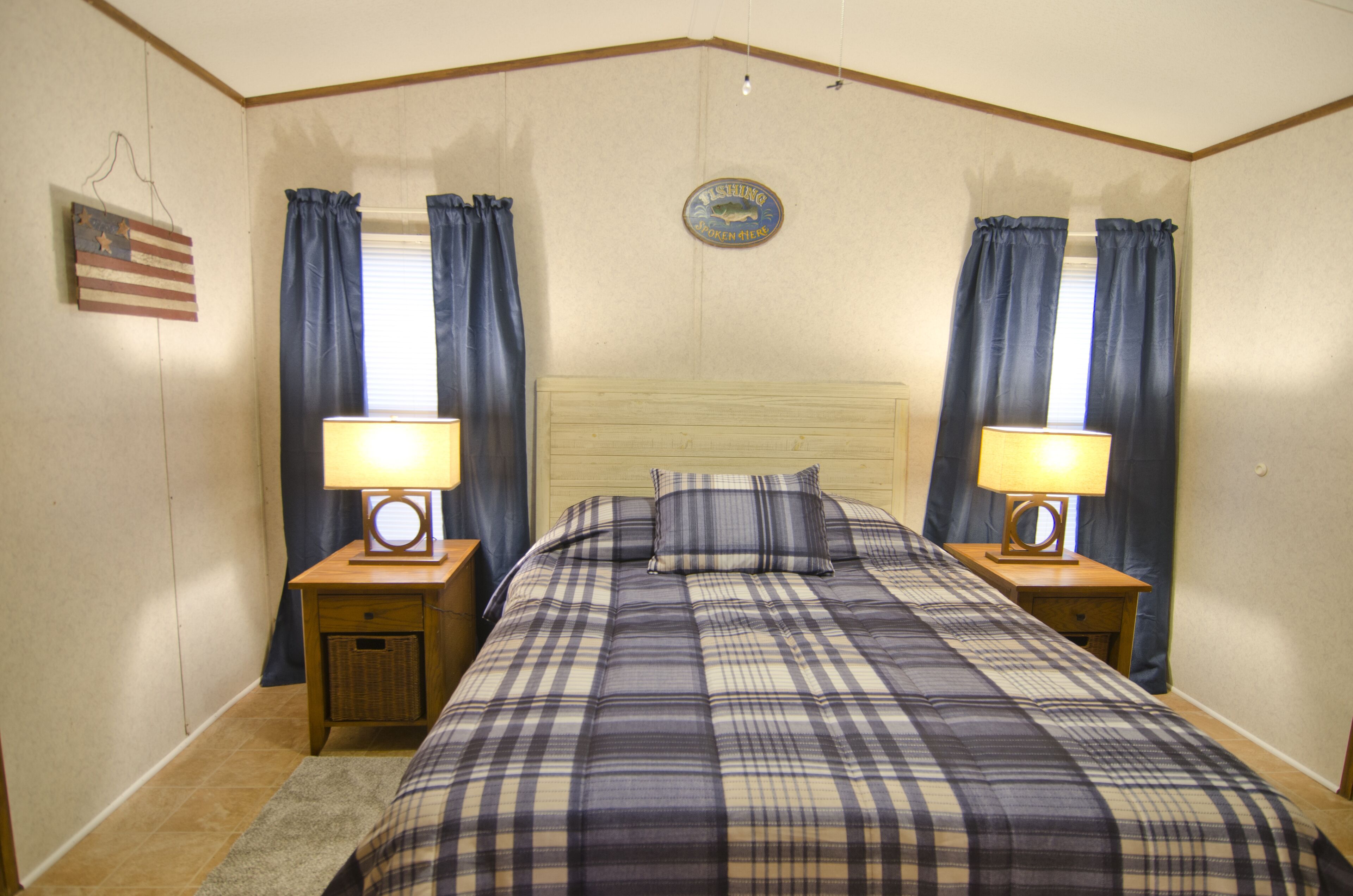 Une chambre à coucher avec une tête de lit en bois, une couvre-lit à carreaux, deux tables de chevet avec des lampes et des rideaux aux fenêtres.