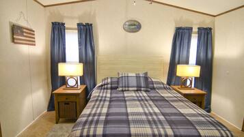 Une chambre à coucher avec une tête de lit en bois, une couvre-lit à carreaux, deux tables de chevet avec des lampes et des rideaux aux fenêtres.
