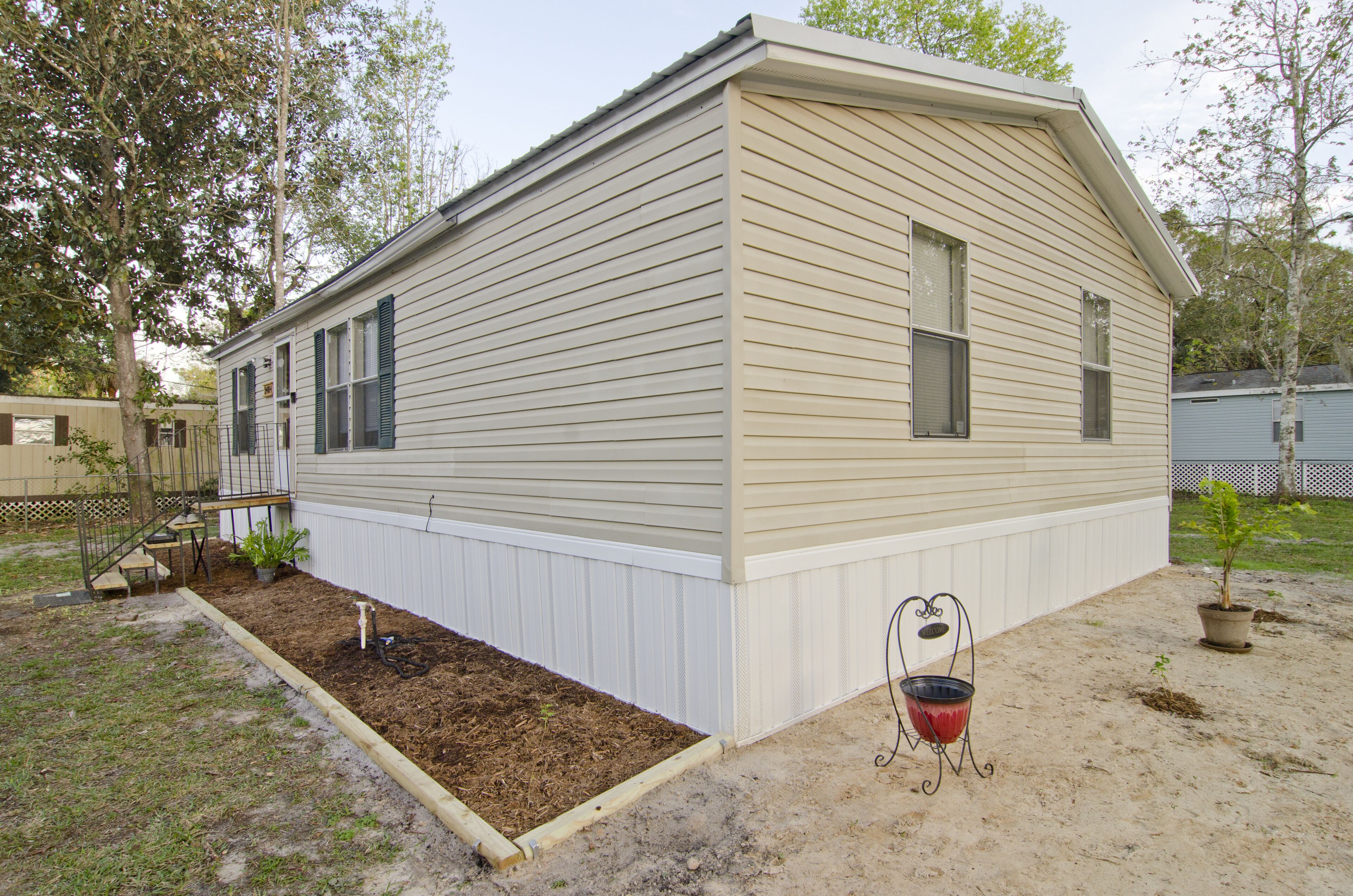 Une maison de plain-pied avec un toit à pignon, un porche à l’avant et un petit jardin agrémenté d’une plante en pot et d’un barbecue.