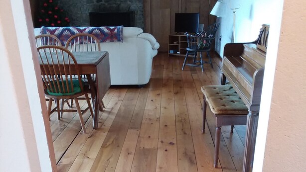 Ett mysigt vardagsrum med en vägg av sten, trägolv, en soffa, ett matbord med stolar och en bänk.